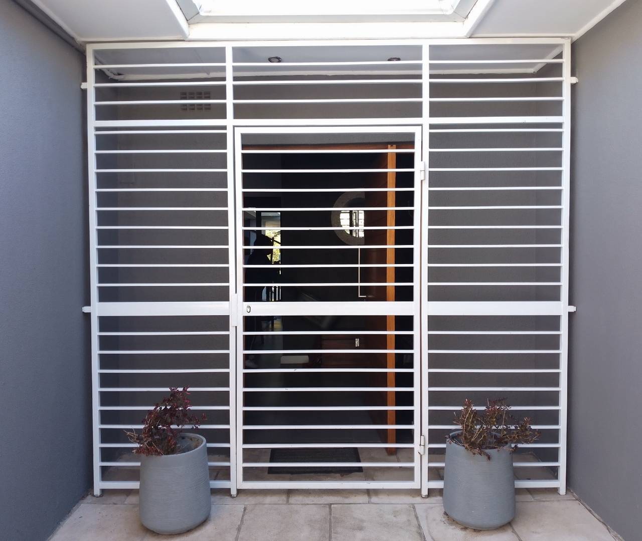 Modern grey swing gates installed in a sleek architectural setting with matching planters.