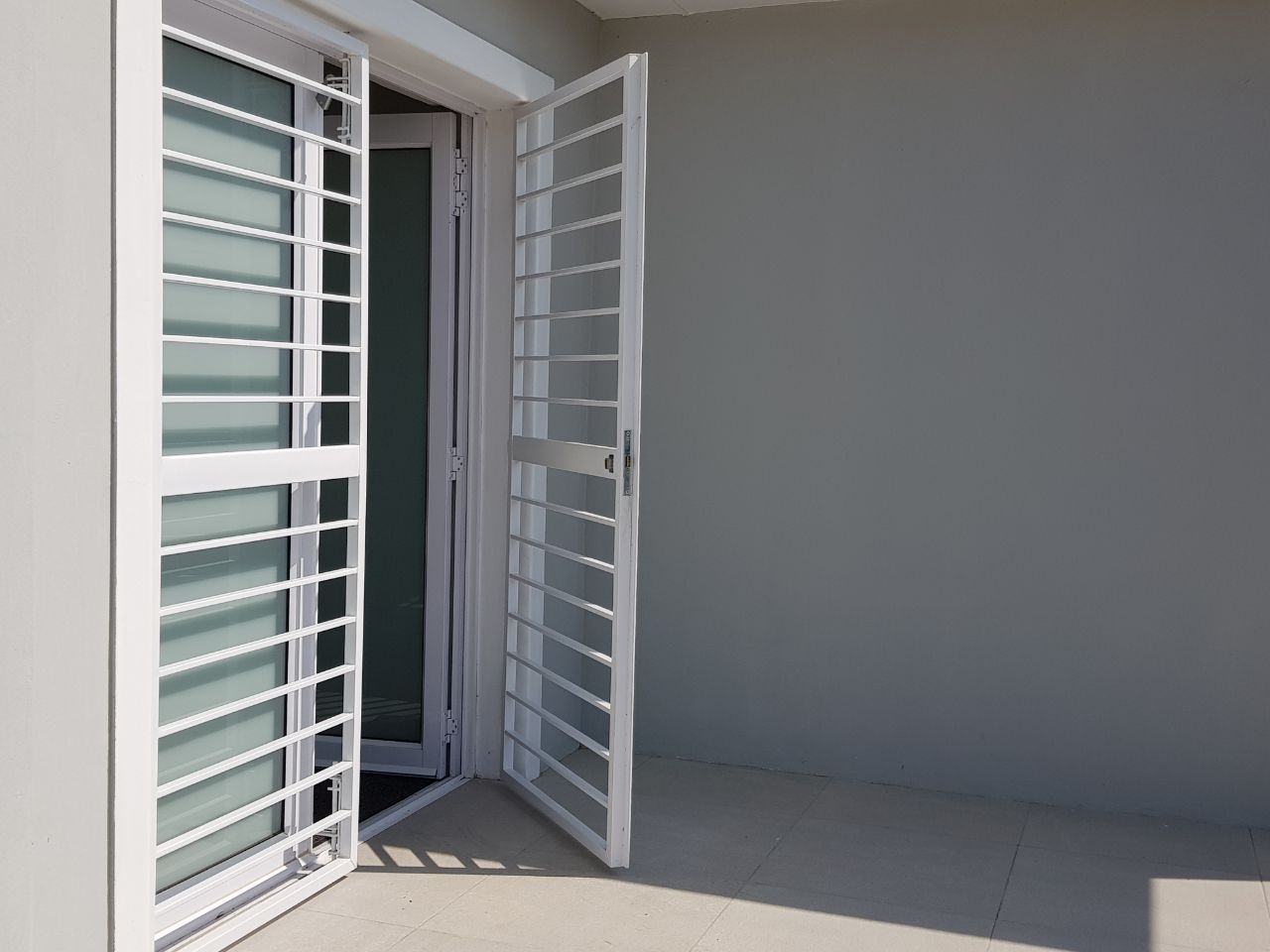 White steel security gate with horizontal bar design, installed on the entrance of a modern home. The gate is ajar to express its style in different dimensions.