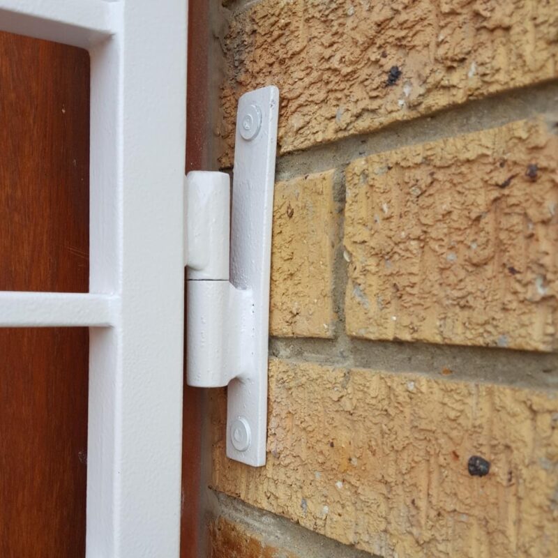 Close-up of white bullet-nose hinge securely fastening steel swing gate frame to brick wall.