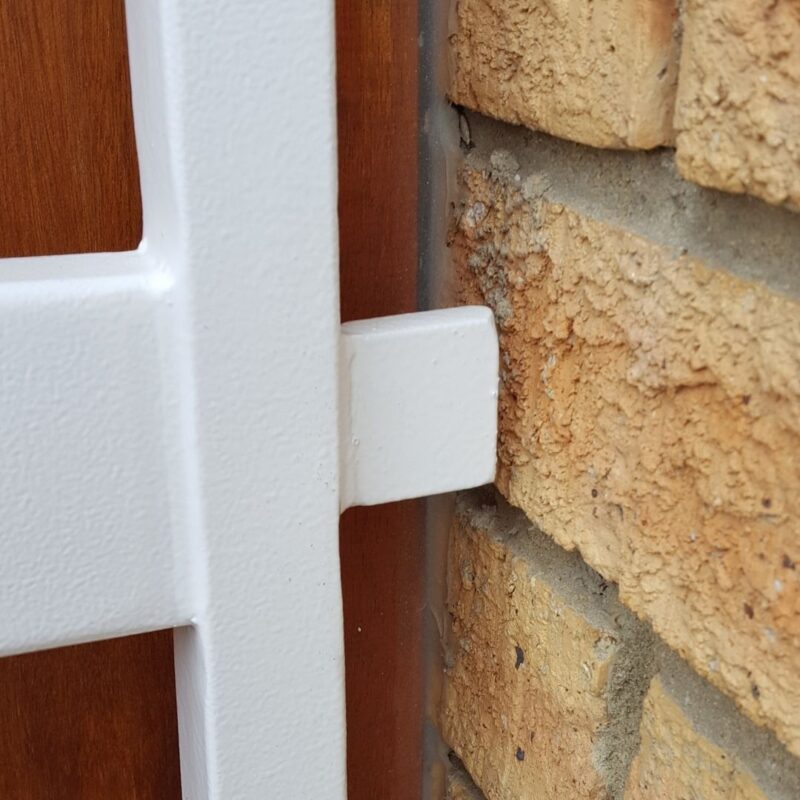 Thick welded stopper bar on steel swing gate preventing over-travel against rustic brick reveal.